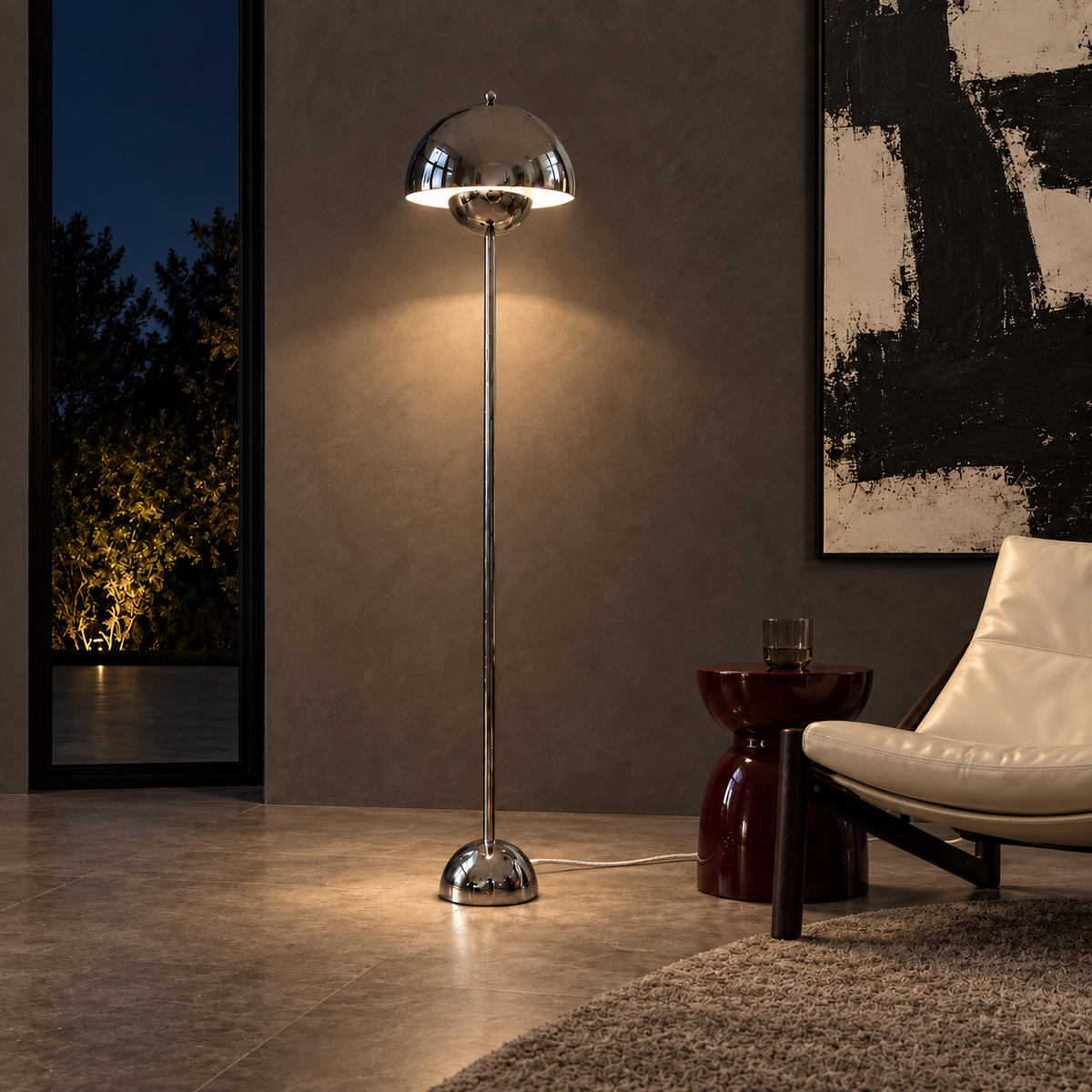 Saturn chrome floor lamp casting warm light in a contemporary charcoal interior at night, beside an ivory lounge chair.
