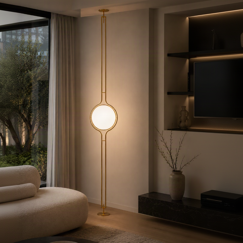 A modern gold floor lamp with a glowing oval light fixture, styled in a warm, contemporary living room next to a beige sofa and window.