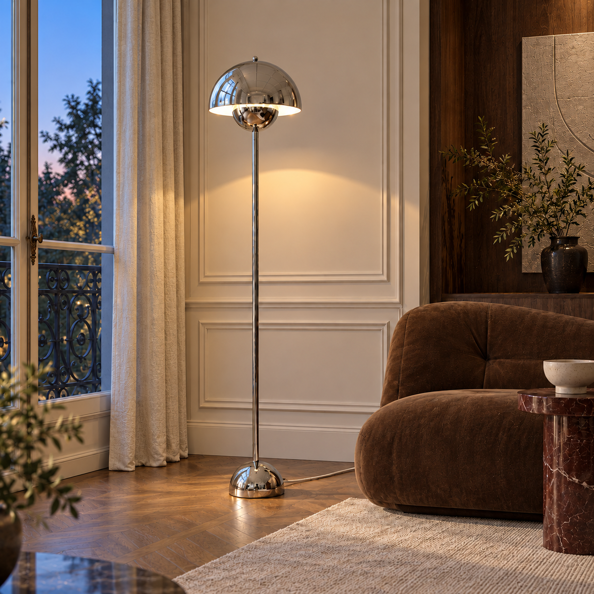 Saturn chrome floor lamp glowing warmly beside a brown lounge chair at dusk, with a subtle white woven cord.